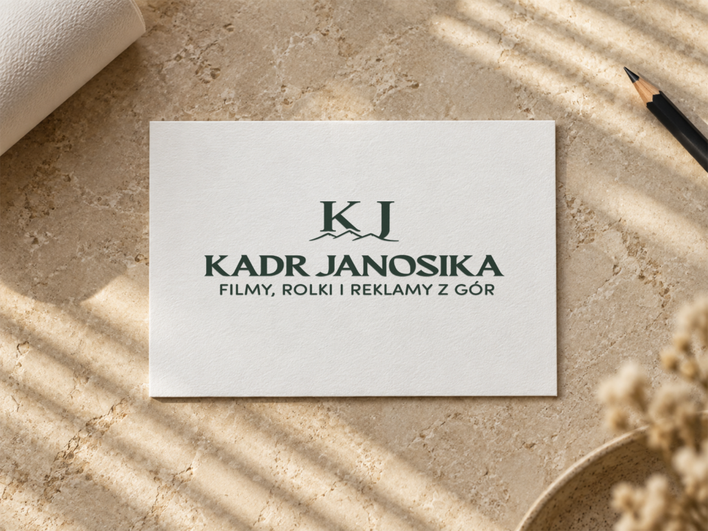 Kadr Janosika – wizualizacja logo marki filmowej. Zielone logo „Kadr Janosika” z motywem gór i podpisem „Filmy, rolki i reklamy z gór” na białej karcie na beżowym kamieniu.