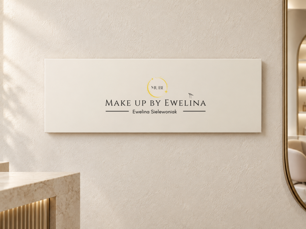 Make Up By Ewelina – wizualizacja logo salonu makijażu Logo „Make Up By Ewelina” na jasnej tablicy w salonie makijażu, obok lustra w szampańskiej ramie.