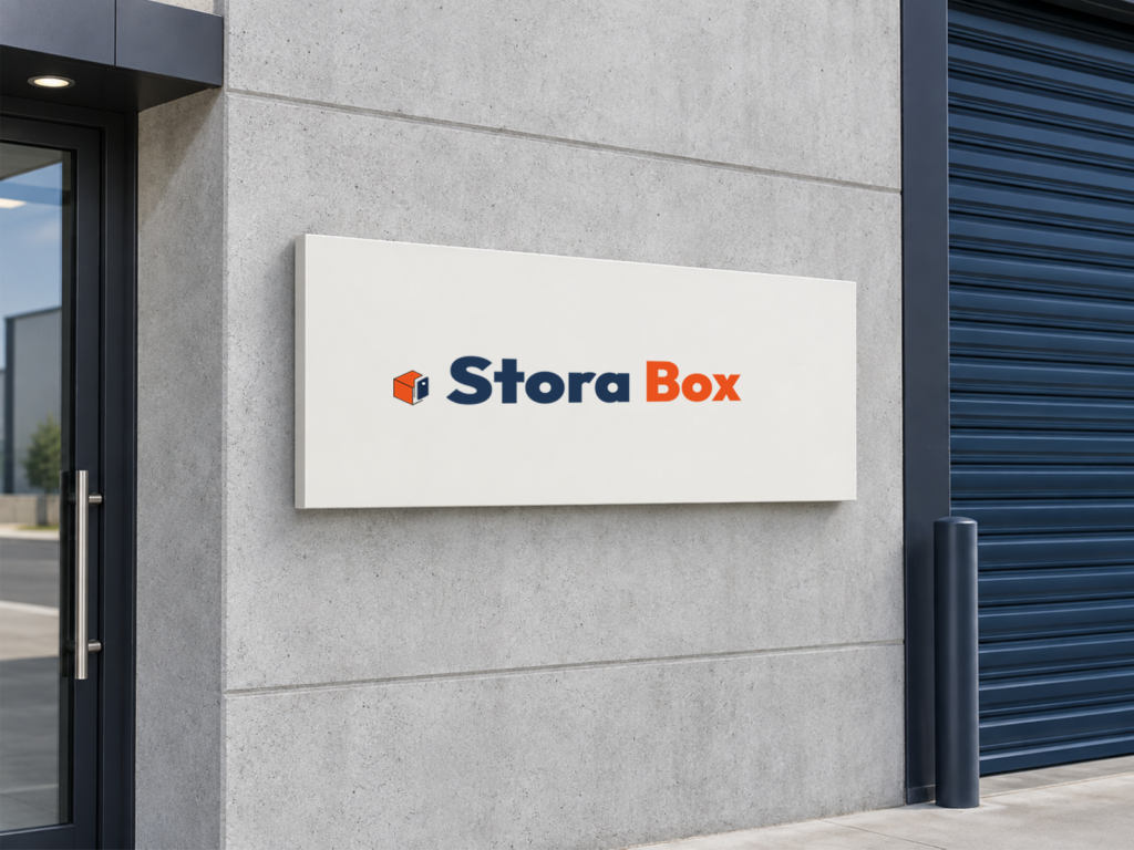 Stora Box – wizualizacja logo firmy wynajmującej magazyny Granatowo-pomarańczowe logo Stora Box na jasnej tablicy przy wejściu do magazynu, obok granatowej bramy.